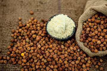 Close up of a jut bag full of chickpeas or grams in it and its floor or besan ka atta in a clay bowl on brown colored surface.