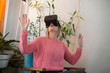 © MexChriss - woman in pink sweater at home enjoying using virtual reality goggles in modern armchair