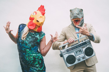 Crazy senior couple wearing chicken and t-rex mask while dancing outdoor - Mature trendy people having fun celebrating and listening music with boombox - Absurd concept of masquerade funny holidays