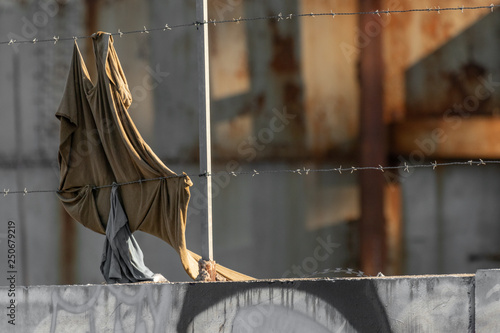 War and political refugees concept. Barbed wire fence detail, torn clothing strips from escape route. European and American closure, closed borders. African, Mexican and middle eastern migration flux.