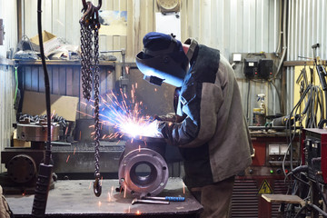 The base for the valve is mounted on the iron table at the factory and the worker welds with a welding machine. Sparks fly. Valve assembly plant