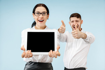 the surprised business man and woman smiling on a blue studio background and showing empty screen of