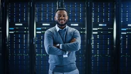 Aufkleber - Bearded Black IT Engineer Standing and Posing with Crossed Arms in the Middle of a Working Data Center Server Room with Server Computers Working on a Rack. 