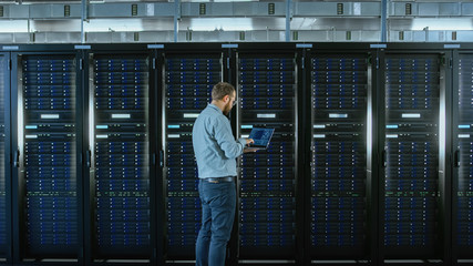 Aufkleber - Bearded IT Specialist in Glasses is Working on Laptop in Data Center while Standing Before Server Rack. Running Diagnostics or Doing Maintenance Work.