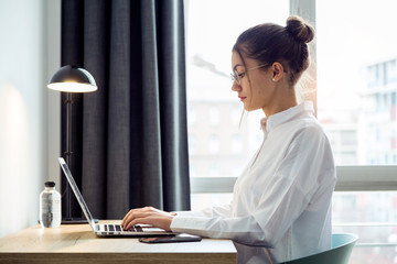 Concentrated beautiful businesswoman working with her laptop on the desk at the hotel room.