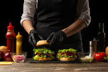 The Chef Prepares A Burger, A Hamburger. On A Background With Ingredients. Delicious And Fast Food, Fast Food. A Menu, A Cafe, Fast Food, Catering, Gastronomy