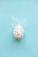 Wall Mural - Traditional easter egg on a blue background in a minimal style with leaves like Easter bunny ears.