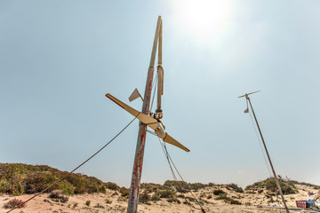 Wall Mural - two small wind turbines, one of them broken, standing on desert, strong back light sun in background