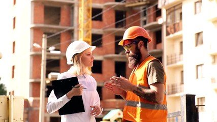 Architect and builder at construction site. Woman engineer and brutal builder communicate construction site background. Construction team communication concept. Discussing plan.
