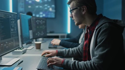 Two Software Developers Programming, Talking and Finding Solutions while Working on Desktop Computers in Data Center System Control Room. Team of Young Professionals Doing High Tech Coding 