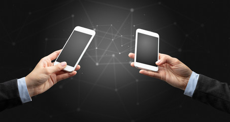 Close up of two hands holding smartphones to each other, wireless connection concept