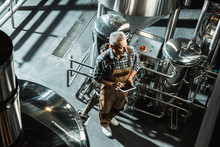 Overhead View Of Brewer In Working Overalls Using Digital Tablet In Brewery