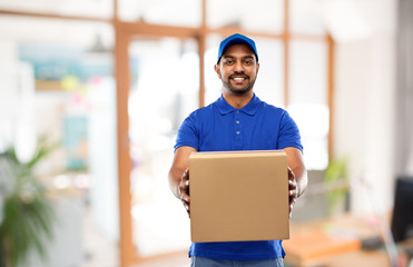 Wall Mural - mail service and shipment concept - happy indian delivery man with parcel box in blue uniform over office background