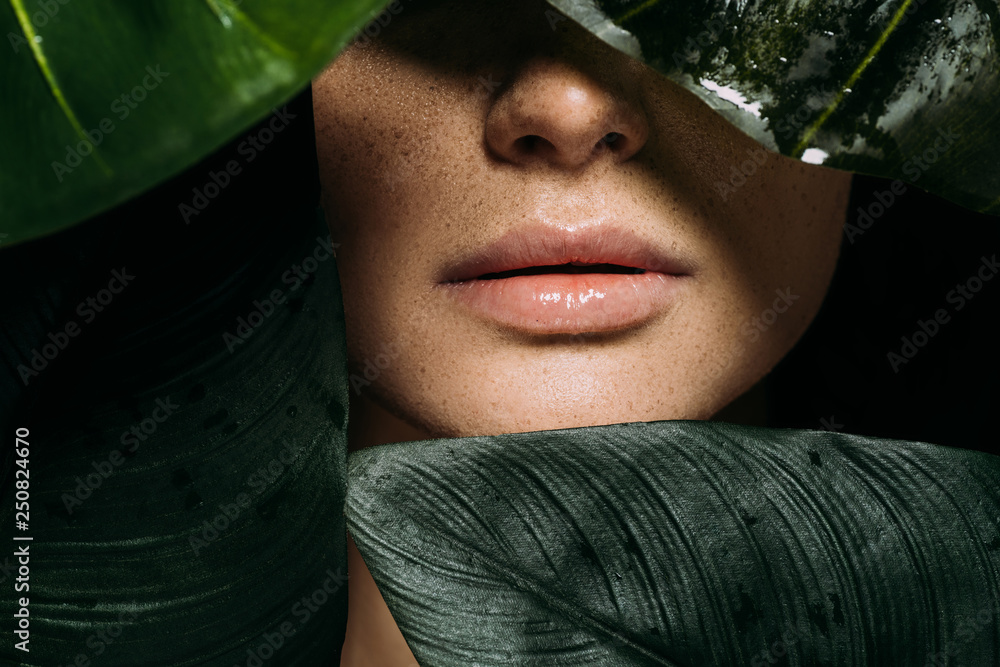 cropped view of girl with freckles posing with green tropical leaves - obrazy, fototapety, plakaty 