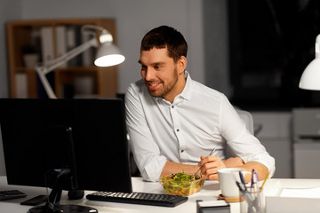 Wall Mural - business, overwork, deadline and people concept - smiling businessman at computer eating vegetable s