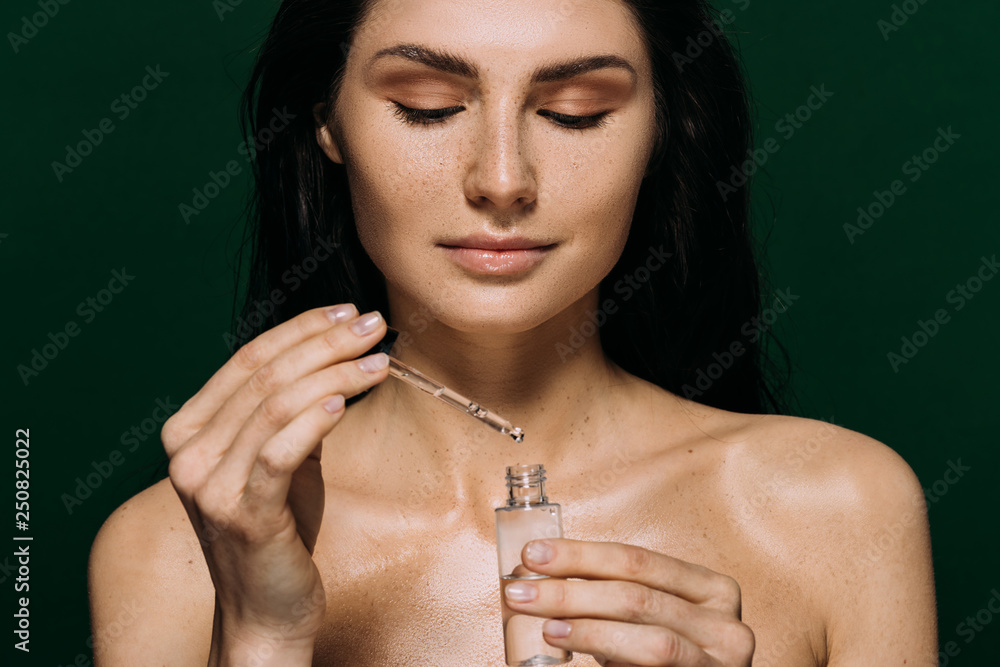 attractive naked woman holding bottle with moisturizing serum isolated on green - obrazy, fototapety, plakaty 