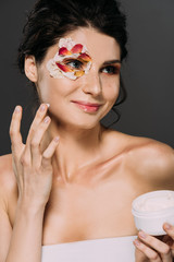 Wall Mural - beautiful smiling woman with petals on face applying moisturizing cream isolated on grey