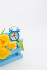 Womans holiday yellow Spring tulips with an alarm clock and blue wooden cart box isolated on white background.Several objects Top horizontal view copyspace