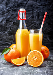 Freshly squeezed orange juice in glass bottle with straw. Fruity still life on black backdrop and grey concrete surface rustic style.