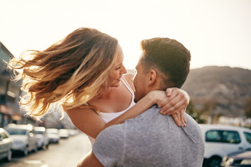 Laughing young couple hugging together on a street at sunset