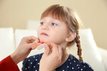 Wall Mural - Nurse applying medical patch to little girl's injured face indoors. First aid