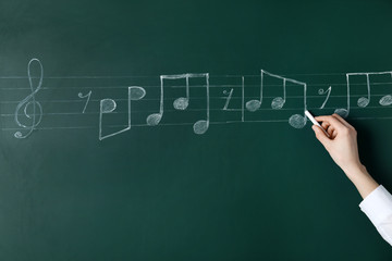 Wall Mural - Woman writing music notes with chalk on blackboard, closeup