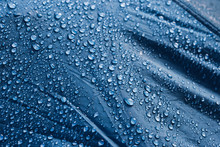 Water Drops On The Fabric. Rain Water Droplets On Blue Fiber Waterproof Fabric. Water Drops Pattern Over A Waterproof Cloth. Blue Background. Dark Blue Rainproof Tent Sheet With Morning Rain Drops.