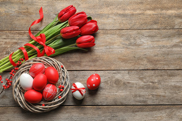 Wall Mural - Flat lay composition of nest with painted Easter eggs and flowers on wooden table, space for text