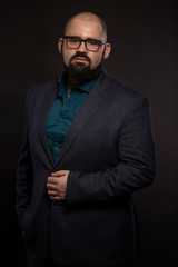 Serious young bald man in glasses with a beard, black background