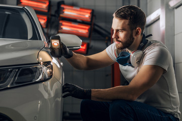 young bearded man has found paintwork defects near the head lamp. close up photo. copy space