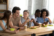 © fizkes - Happy smiling friends sitting together in cafe, using phones