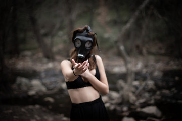 Wall Mural - Anonymous woman in black clothes and gas mask standing in amazing spooky forest