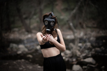 Wall Mural - Anonymous woman in black clothes and gas mask standing in amazing spooky forest