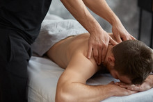 Young Handsome Man Enjoying A Back Massage. Professional Massage Therapist Is Treating A Male Patient In Apartment. Relaxation, Beauty, Body And Face Treatment Concept. Home Massage.