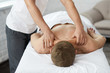 © YURII MASLAK - Young handsome man enjoying a back massage. Professional massage therapist is treating a male patient in apartment. Relaxation, beauty, body and face treatment concept. Home massage.