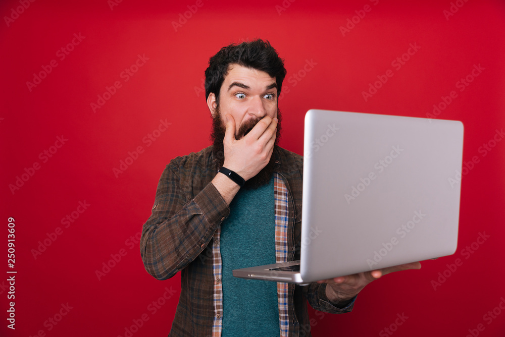 Amazed man holding laptop computer and covering mouth with hand over ...