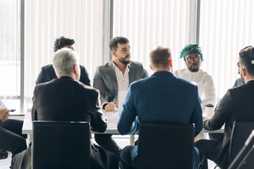 Multiracial group of male experts analyzing business results, close up of team with smartphones and tablet pc sitting at table in office, actively speaking, engaging with each other and working