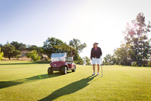 Portrait Of Female Golfer Standing By Golf Cart On Golf Course 