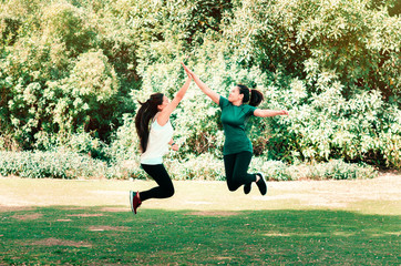 Two female friends giving high five while jumping in the air