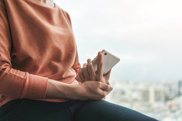 Young asian woman holding her smartphone near window with city view , Selective focus.