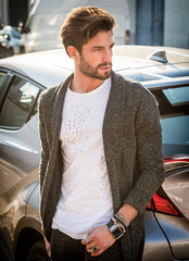 Portrait of young attractive man in white shirt leaning on his new stylish polished car outdoor in city street