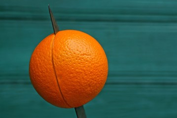 round orange on a sharp knife on a green background