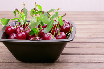 Wall Mural - Black plate of ripe cherries with green leaves on a wooden table