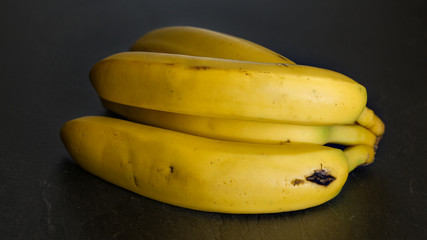 Wall Mural - Closeup - bunch of yellow bananas on black board / background.