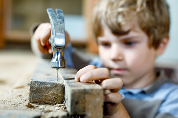 happy little kid boy helping with toy tools on construction site. Funny child of 7 years having fun on building new family home. Kid with nails and hammer. Selective focus on hands and tools.