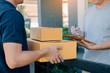 © wutzkoh - Delivery young man standing at the door of home and carrying parcels for young male to signing.
