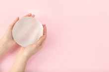 Woman holding silicone implant for breast augmentation on color background, top view with space for text. Cosmetic surgery