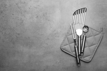 Different kitchen utensils and potholder on grey background, top view with space for text