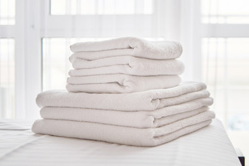 Stack of white clean bath towels on bed sheet in modern bedroom interior, copy space. Close up