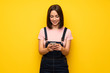 © luismolinero - Young woman over yellow wall sending a message with the mobile